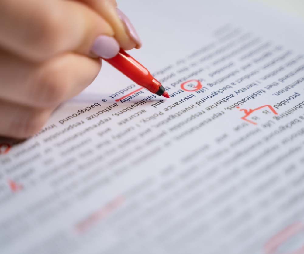 A person is writing on a piece of paper with a red pen
